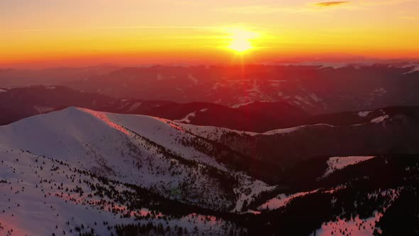 Flying above Winter mountain. During Sunrise or Sunset. Red, orange colored Sky. 