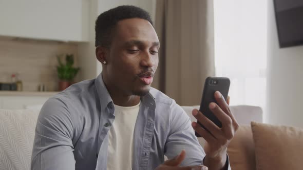 Happy African American Guy on a Video Call and Waving His Hand in His Apartment Using Smartphone