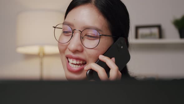 Smiling of young Asian woman calling phone and talking with friends while working at home.