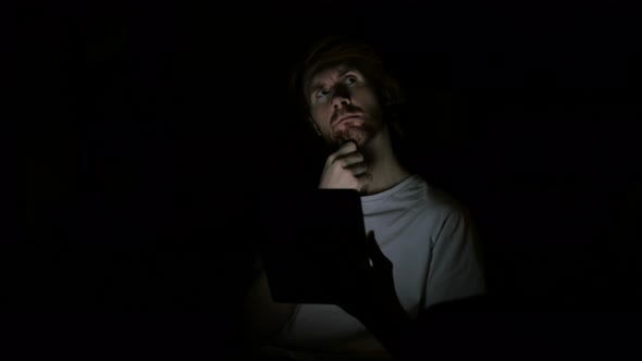 Redhead Man Thinking and Working on Tablet at Night