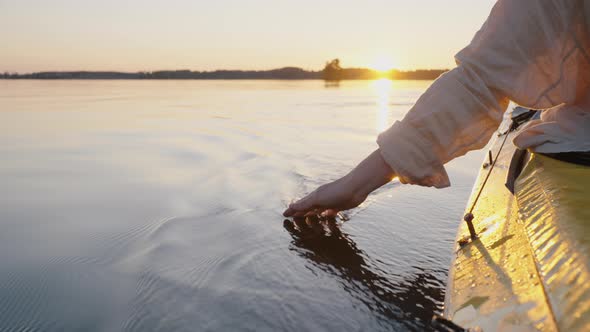 Person Sails on Canoe Touching Water with Hand Making Waves