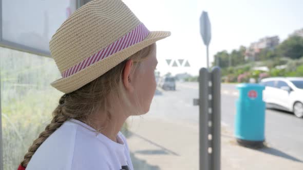 Little Girl Sitting on a Bench Waiting for Transport at the Bus Stop.