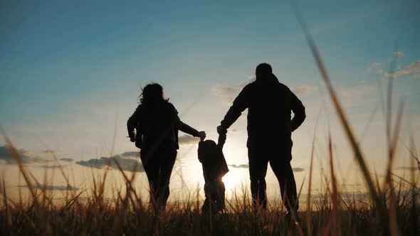 Happy Young Family Together with Their Little Child at Sunset. Parents Raising Baby Up in the Air