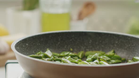 Crop woman putting green beans on plate in kitchen