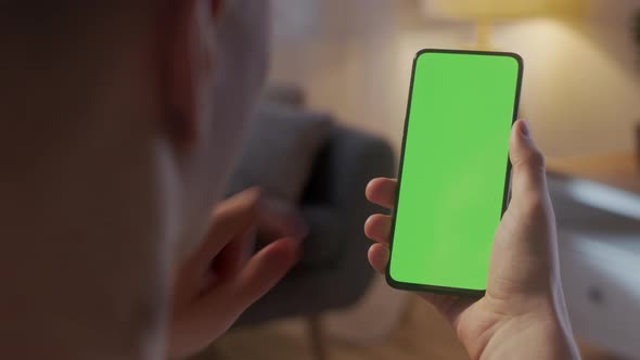 Handheld Camera Back View of Blond Man Holding Chroma Key Green Screen Smartphone Watching Content