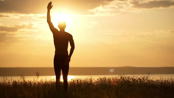 Silhouette of Young Sportive Man Practicing Yoga at Sunset