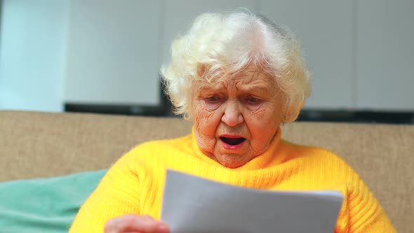 Shoked Amazed Old Woman White Grayhaired Sitting on the Sofa in Living Room with Bills