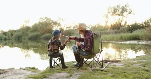 Grandpa in Straw hat which Drinking Tea Together with his Grandchild on the Pond where they Fishing