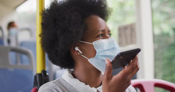 African american businesswoman with face mask talking on smartphone and sitting in bus