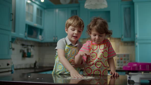 Two kids in aprons playing with dough on kitchen table at home. Children tasting raw dough