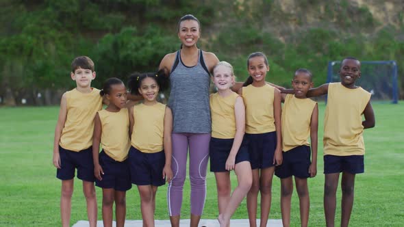 Portrait of mixed race female teacher and diverse group of schoolchildren smiling embracing outdoors