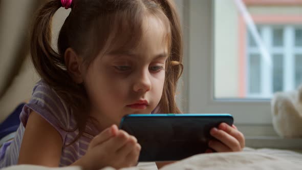 Little Girl Using a Smartphone is Watching the Internet in the Bedroom