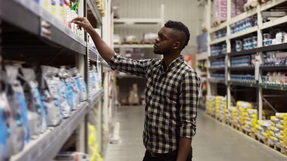 A Man Walk Along the Shelves in the Store and Choose a Product