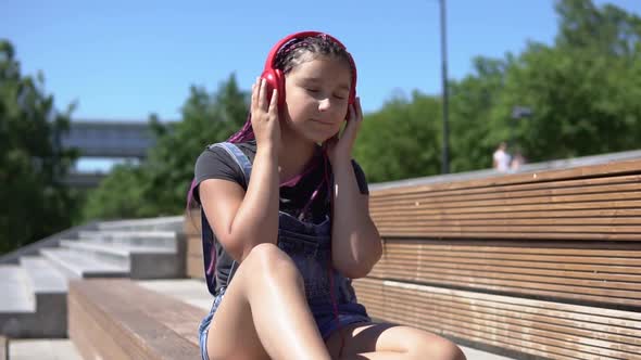 Girl Listening to Music on Headphones Sitting on a Bench in Summer Park