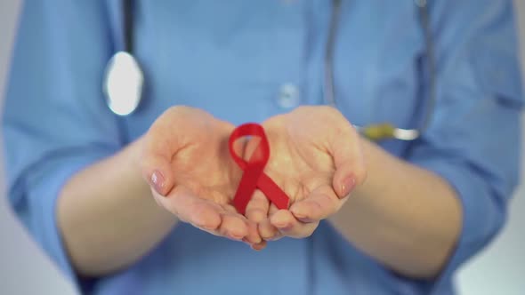 Female Gynecologist in Blue Coat Holding Red Ribbon in Palms, AIDS Awareness