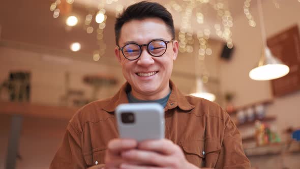 Laughing Asian young man wearing eyeglasses typing on phone