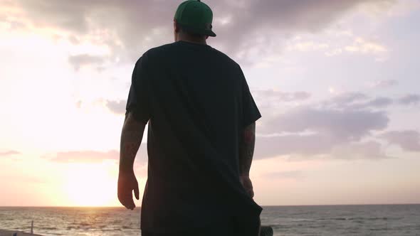 Young Man with Skateboard Looking on the Sea During Sunrise