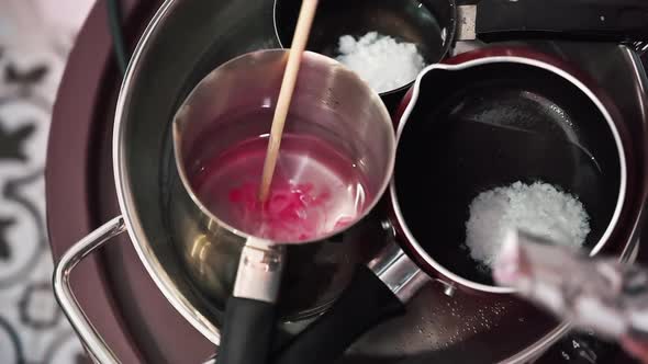 Hand made candles production, female hand mixing dye and melting wax in pots. Slow motion