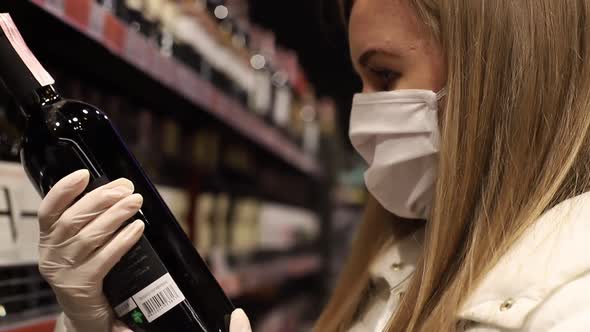 Young woman in medical mask selects wine in supermarket buying products .