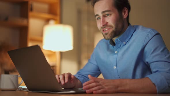 Smiling man texting on laptop in office