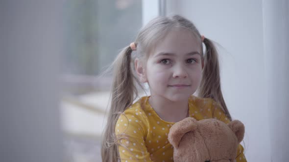 Close-up Portrait of Cute Little Girl in Yellow Dotted Dress Holding Teddy Bear. Pretty Caucasian