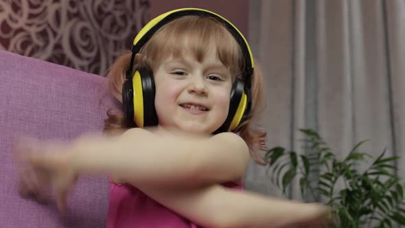 Little Child Girl in Headphones Enjoying Listen Music. Dancing on Sofa at Home