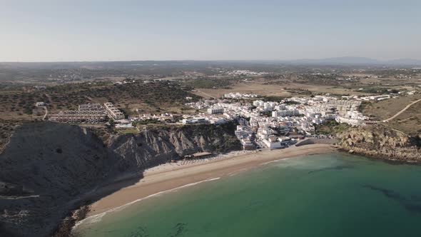 Burgau Beach surrounded by rocky cliffs, calm emerald Atlantic ocean. Aerial establisher