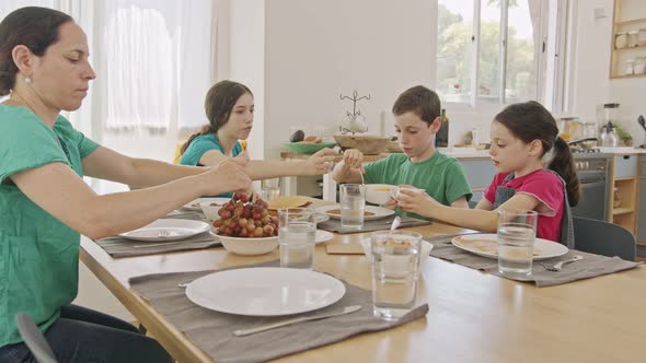 Mother and three kids eating breakfast of pancakes and fruits