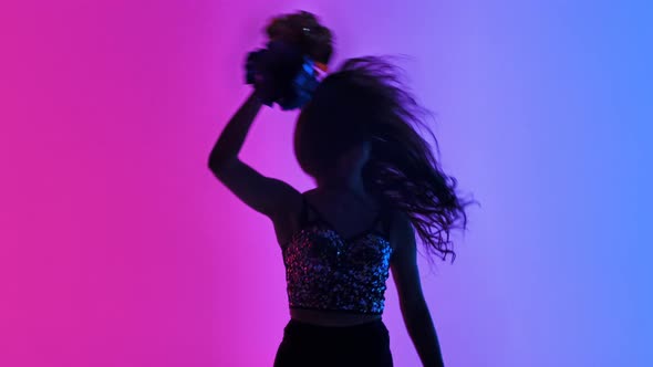 Silhouette of Slender Cheerleader Dancing Energetically with Pompoms in Hands Against Background of