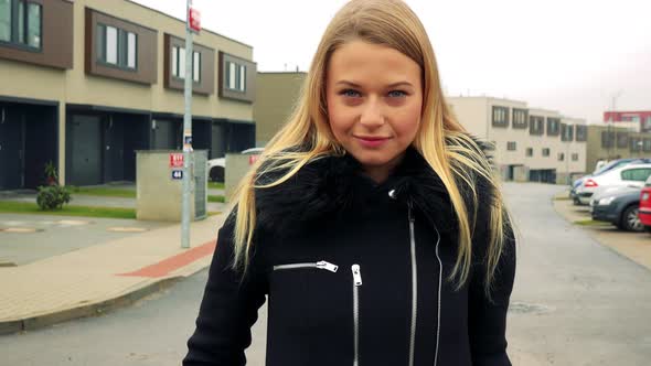 A Young, Beautiful Woman Stands on the Street and Looks at the Camera, Buildings in the Background