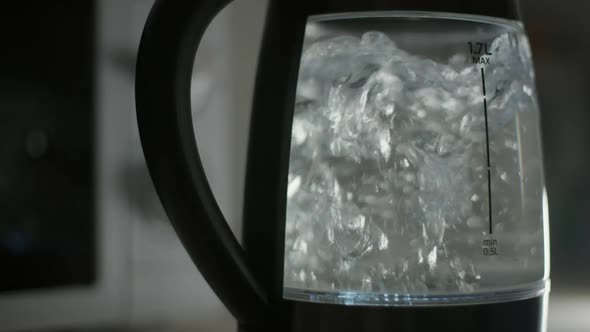 Closeup Electric Kettle with Water Bubbles Boiling in Dark Kitchen at Home