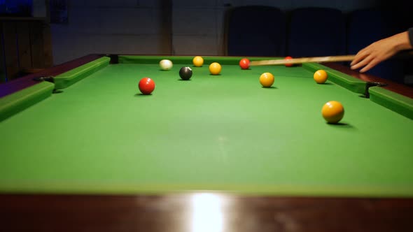 Slider shot of pool player potting a yellow ball on a pol table in a pub bar