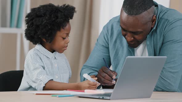 Little African American Kid Schoolgirl Sitting at Desk Doing Homework Mature Dad Helps Daughter with