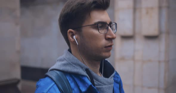 Stylish Guy with Glasses Goes and Listens to Music with Headphones