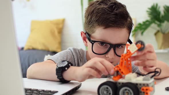 Boy holds the robot car and fixes the sensor chip.Child learns coding, programming and robotics.