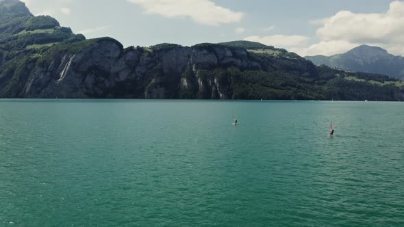 Two Men are Windsurfing on a Lake at the Foot of the Alps in Switzerland