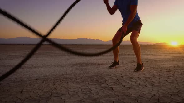 Athletic man working out with battle ropes on a dry lake at sunset