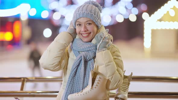 Middle Shot Portrait of Cheerful Beautiful Young Caucasian Woman Posing with Ice Skates and Blurred