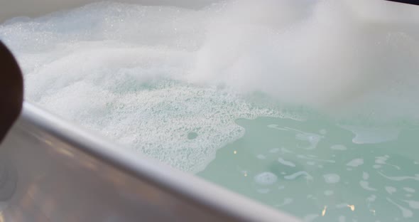 African american woman getting into bath with one leg in bathroom