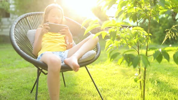 Happy kid girl playing game on mobile phone in the park outdoor