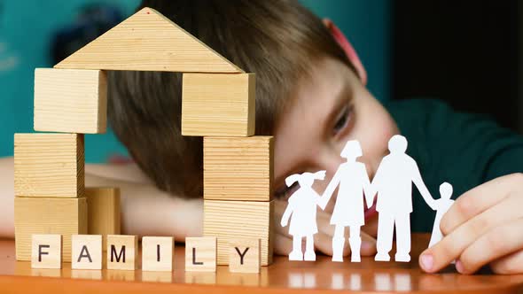 A caucasian boy of 6-7 years old holds a paper-cut silhouette of a family in his hands. Inscription