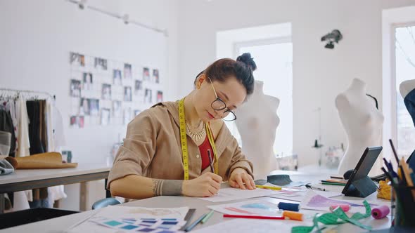 Young Woman in Eyeglasses Designing Clothes Working on New Garment Collection in Designer's Workshop