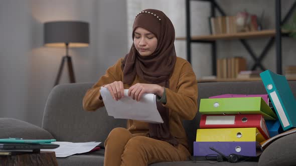 Angry Overwhelmed Slim Woman in Hijab Tearing Documents Crossing Hands Sitting on Couch in Home