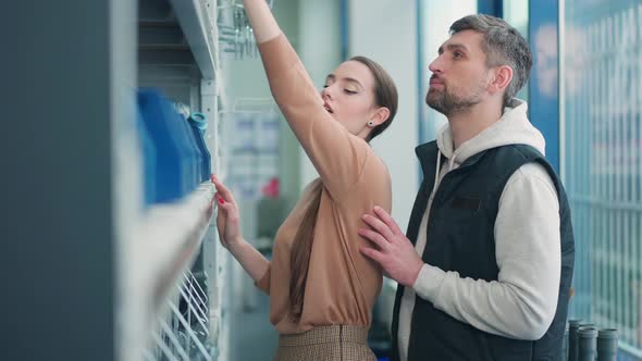 Side View of Charming Slim Beautiful Woman Choosing Pipe Connector with Man in Hardware Store