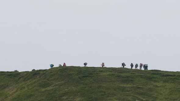 Group of Tourists with Hiking Backpacks Climbs the Mountain Range, Afar View