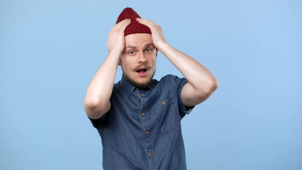 Portrait of Upset Man with Curly Mustache and Hat Expressing Grabbing His Head in Panic Isolated