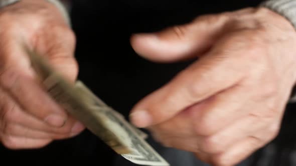 An elderly man holds a small amount of dollar bills.