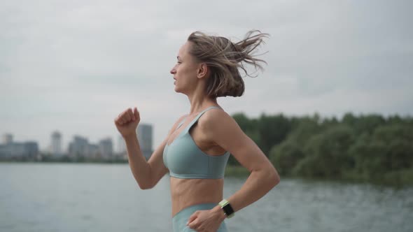 Slow Motion Young Sportswoman in Sportswear Trains in a Park Near the River