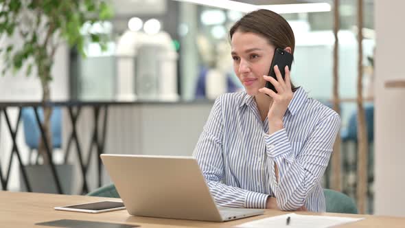 Young Woman with Laptop Talking on Smartphone in Office 