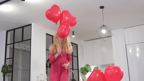 Little Girl Jumping with Red Heart Shape Balloons at Home